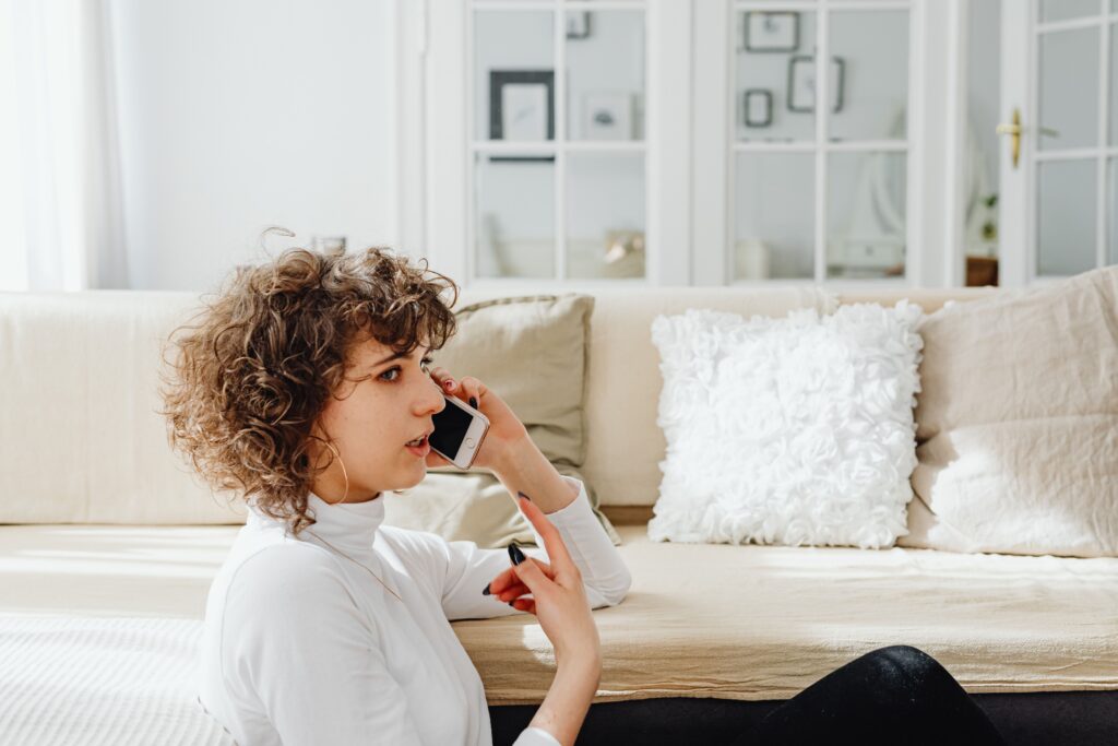 A woman sitting on the floor talking on her phone with a concerned expression, representing trying to find out who you are talking to and identifying unknown callers online.