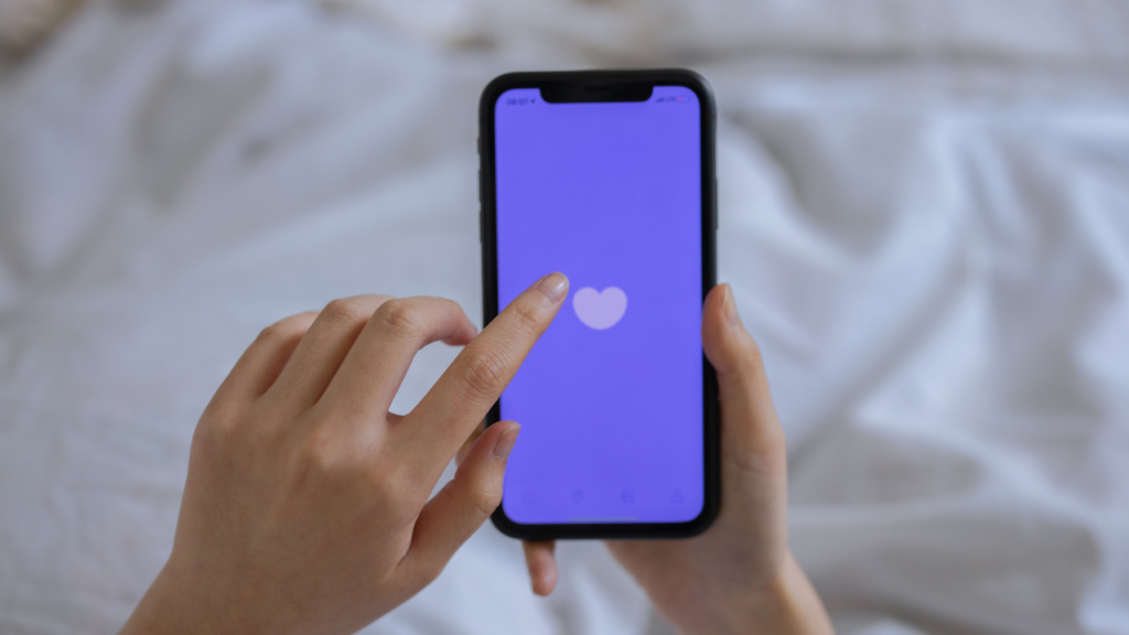 Hands holding a smartphone tapping the Badoo app's heart icon on the loading screen