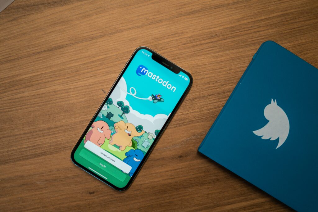 Phone displaying the Mastodon app login screen next to a Twitter-branded notebook, symbolizing the migration from Twitter to Mastodon