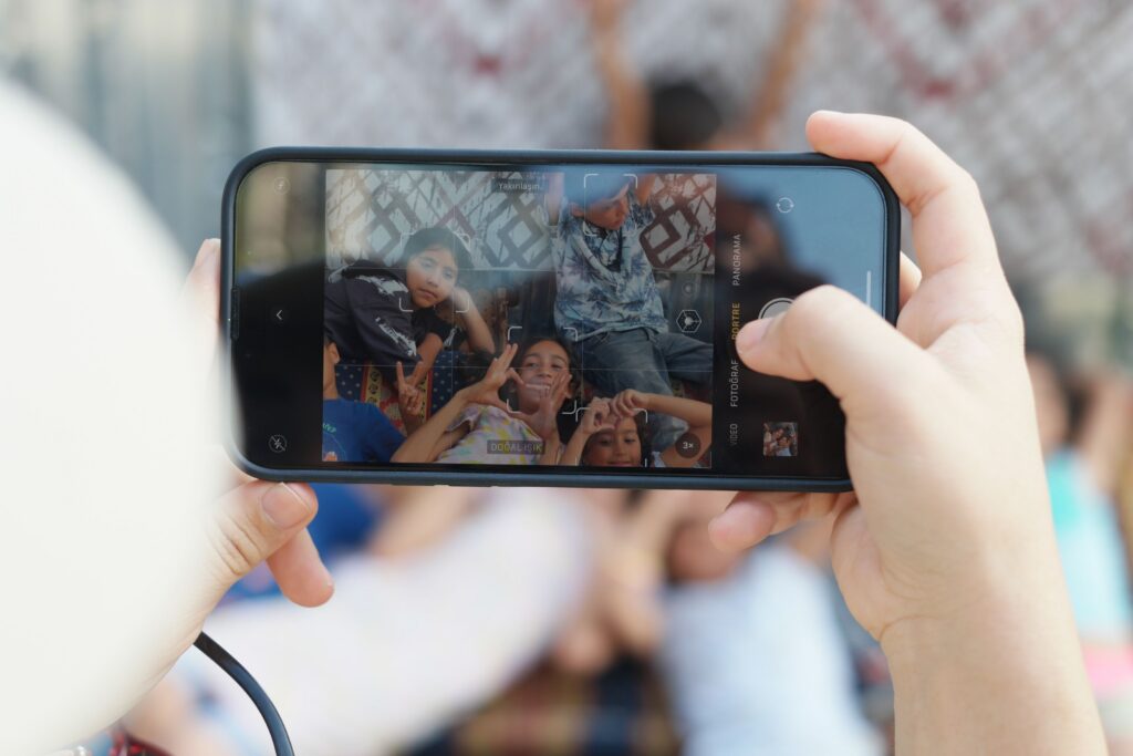 Smartphone camera screen capturing a group of children posing together outdoors, making peace signs and heart hand gestures.