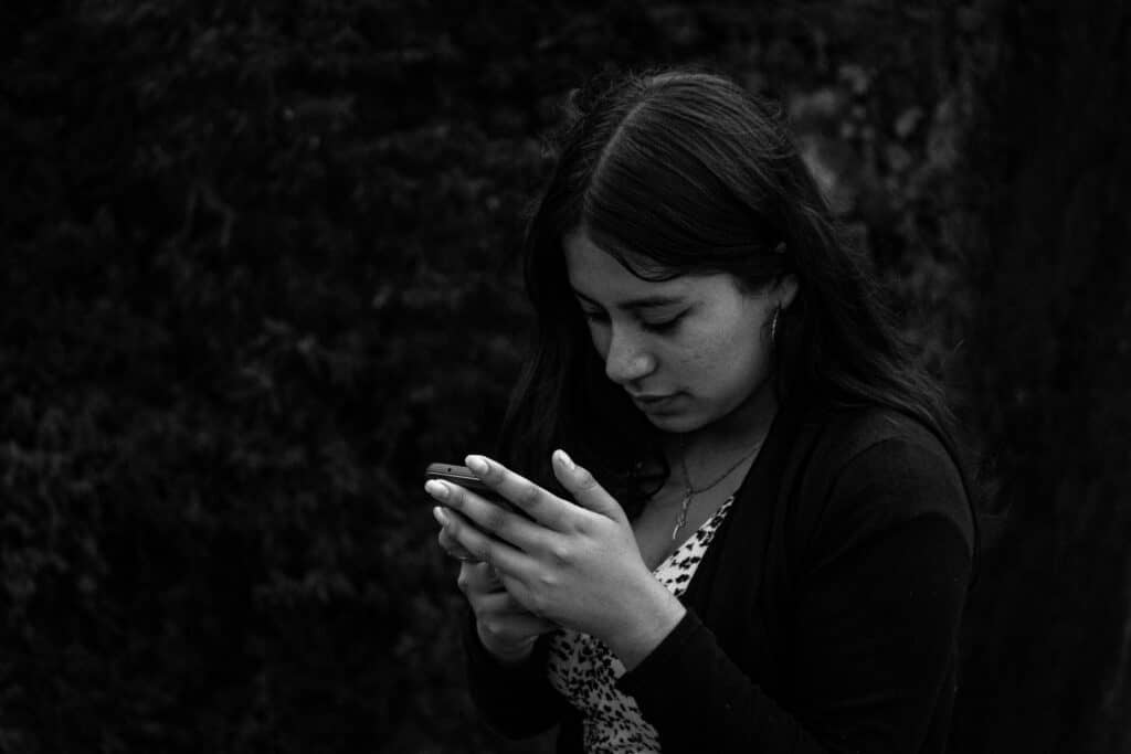 Black and white close-up of a young woman texting on her phone outdoors, focused intently on the screen