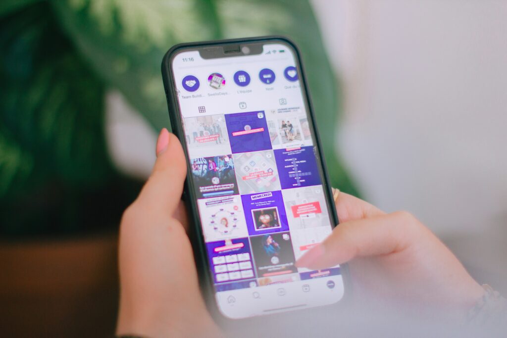 Hand holding a smartphone showing an Instagram profile grid with story highlights and colorful social media posts.
