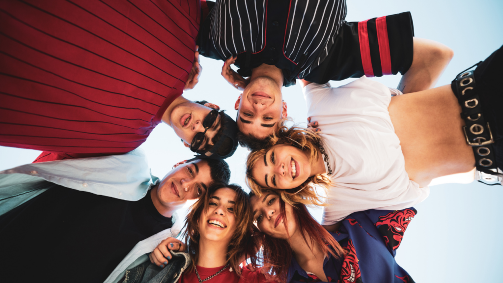 Group of college-age friends huddled in a circle, smiling and looking down at the camera, illustrating the Fizz app's campus social community.