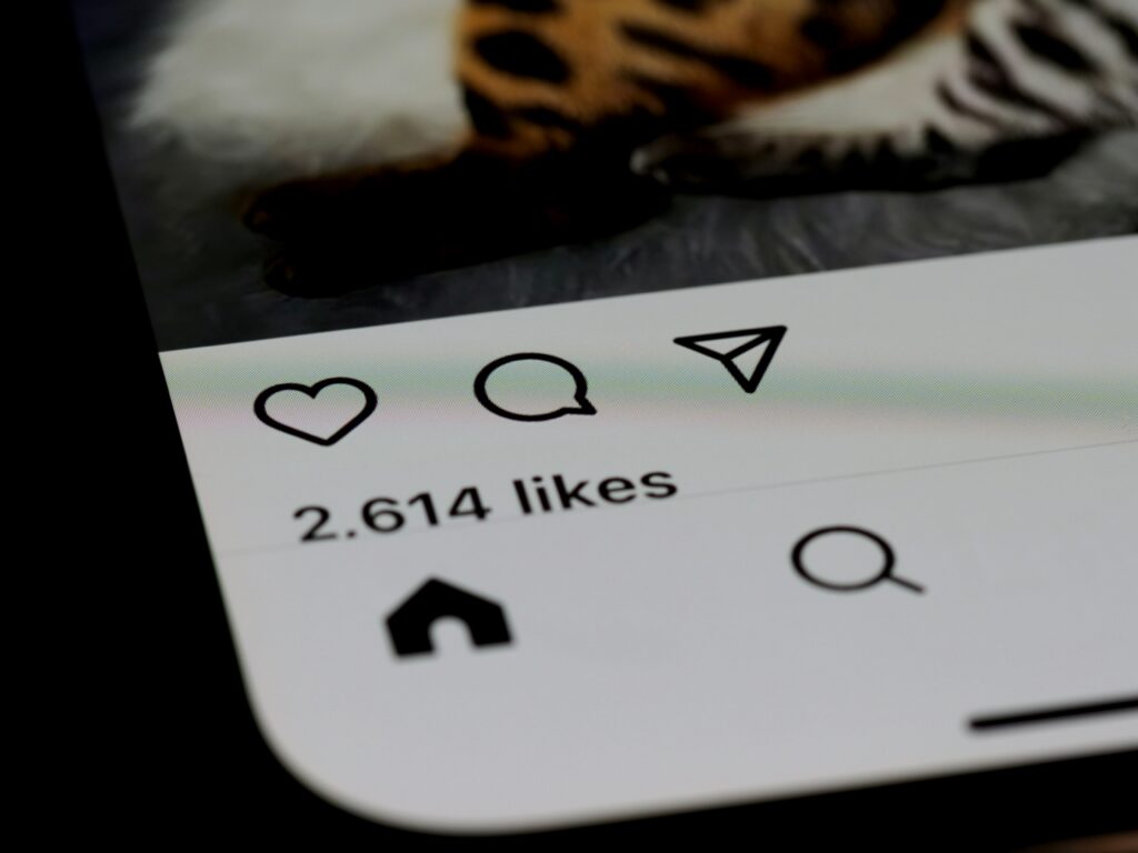 Close-up of a smartphone screen displaying Instagram's like, comment, and share icons above a "2,614 likes" count, with a blurred leopard-print background.