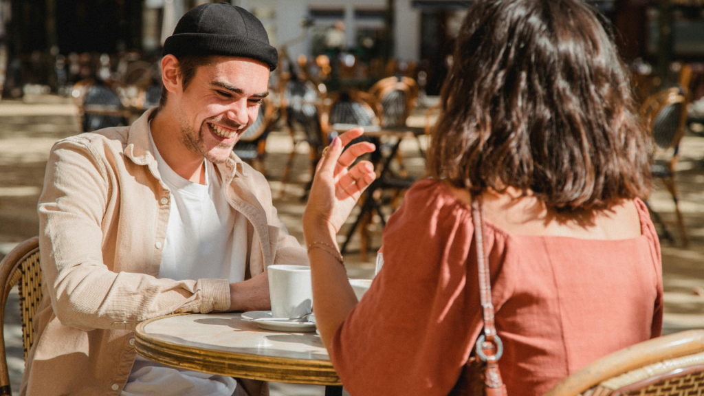 Man and woman on a first date at an outdoor café table, laughing over coffee