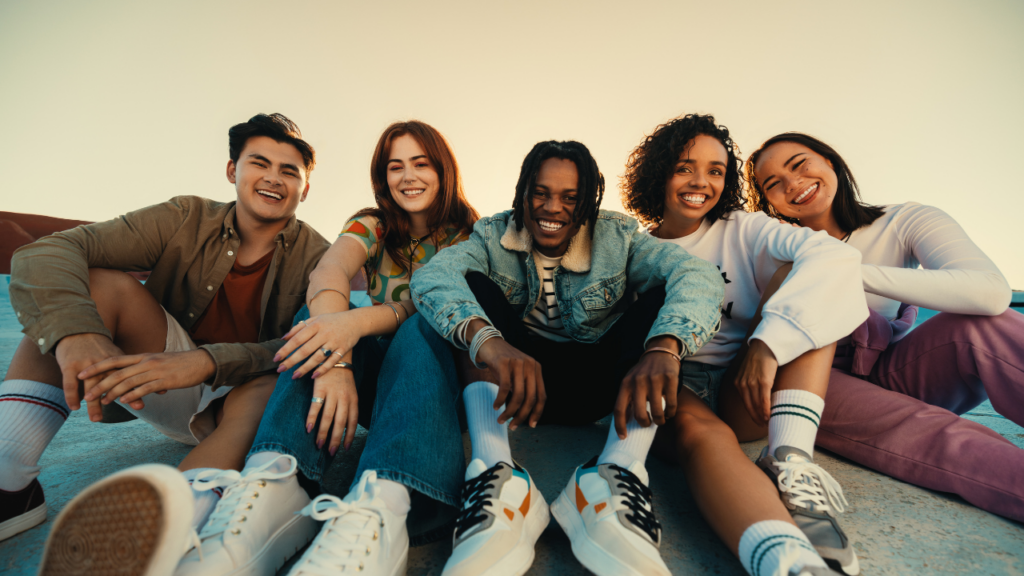Group of five friends sitting together outdoors, smiling at the camera