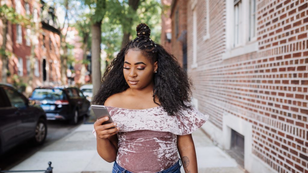 Woman walking on a city sidewalk while looking at her phone