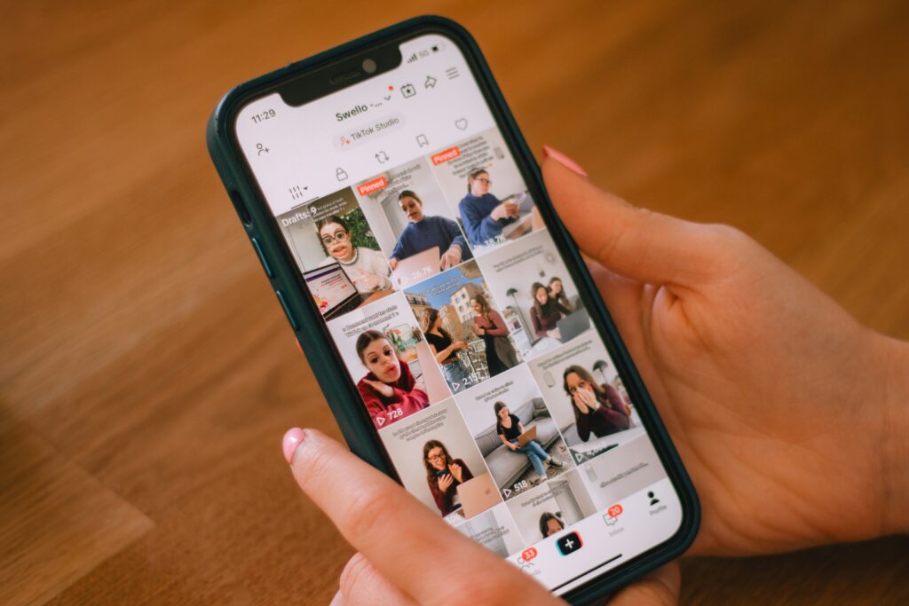 A person holding a phone displaying a TikTok content grid with view counts and a pinned video, managed through a social media scheduling tool.