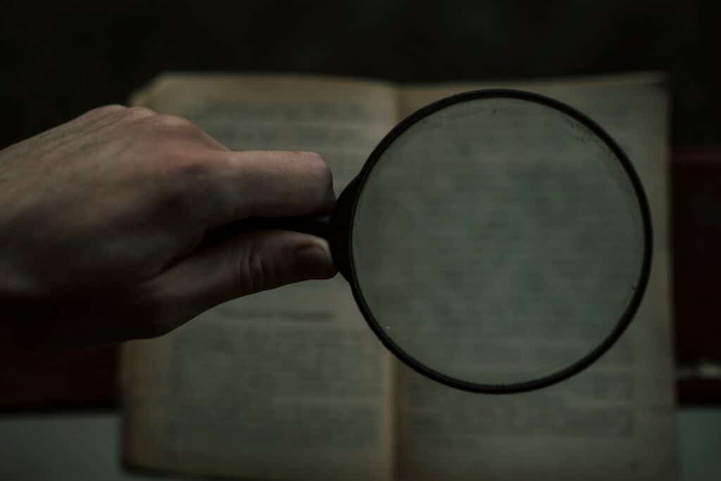 Close-up of a hand holding a magnifying glass over an open, weathered book, symbolizing close examination and research.
